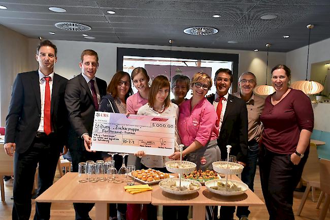 Checkübergabe. Zenzünen Christian, Schmid Flavio (beide UBS), Bayard Rafaela, Ruppen Anina, Winter Monika, Winter Jossen Elisabeth, Imboden Reinke Sarah (alle Zuckerpuppa), Fux Marcel (UBS), Reinke Thomas (Präsident Stiftungsrat), Short Petra (Zuckerpuppa) freuen sich über den Ausbau und die Förderung.