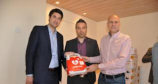 Dr. Aron Pfammatter von coeur wallis (links) und Diego Lareida von der Kantonalen Walliser Rettungsorganisation (rechts) &uuml;bergeben dem Gemeindepr&auml;sident von Veyras, St&eacute;phane Ganzer, einen Defibrillator.