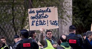 Ein &laquo;Gelbwesten&raquo;-Demonstrant h&auml;lt ein Plakat mit der Aufschrift &laquo;Guignols (Dummk&ouml;pfe) regieren Frankreich! SOS!&raquo;.