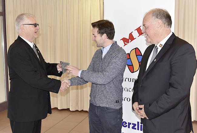 Dank. Tony Jossen überreichte «Belalp»-Dirigent David Lochmatter einen Pflasterstein des Römer Petersplatzes, auch Kassier Roland Walker freute sich.  Foto mengis media